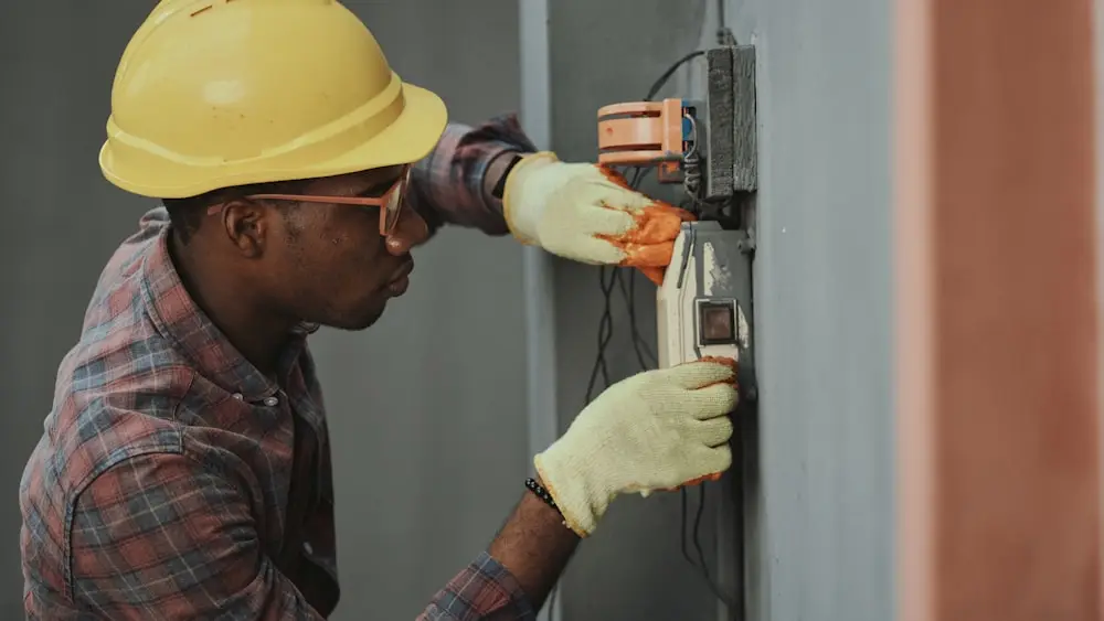 An electrician in a hard hat working inside an electrical panel