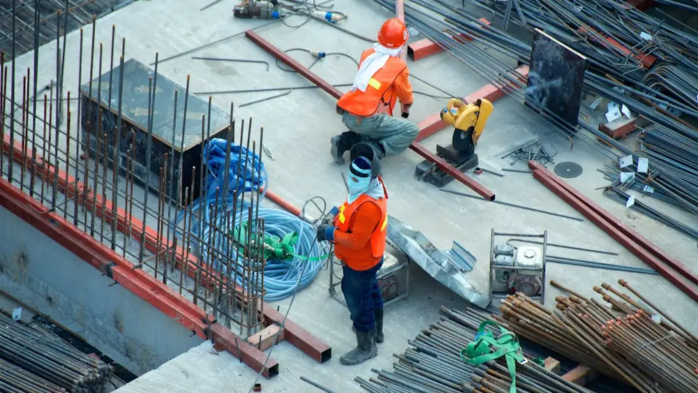 Workers in high-visibility gear tying rebar on a construction deck