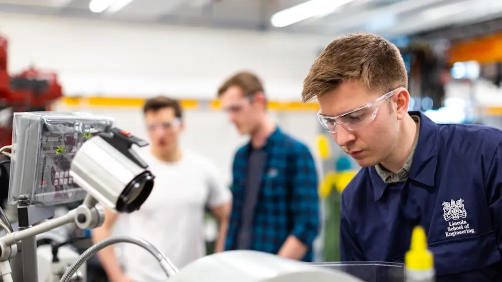 Trainees in safety glasses gathered around a machine in a workshop