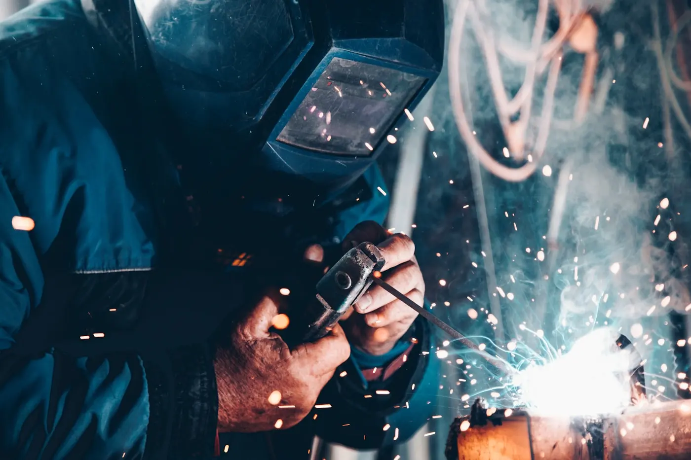 A welder in a face shield working, sparks flying from the joint