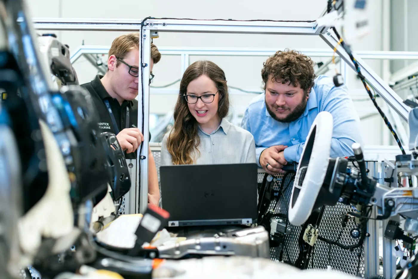 Three engineers reading test data from a laptop at a workbench