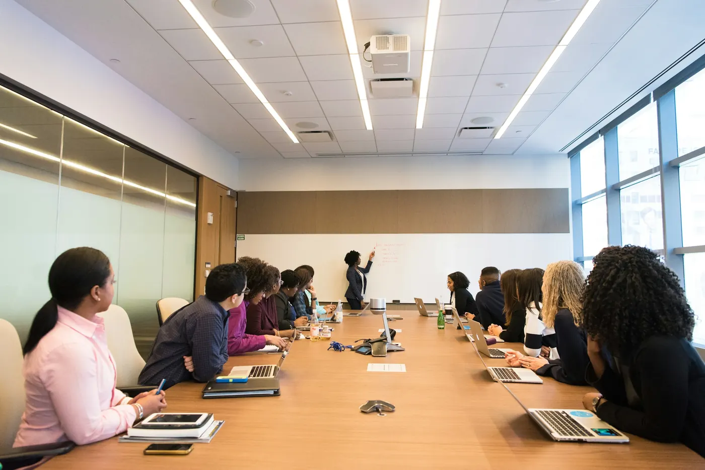An engineer presenting at a whiteboard to colleagues seated around a meeting table